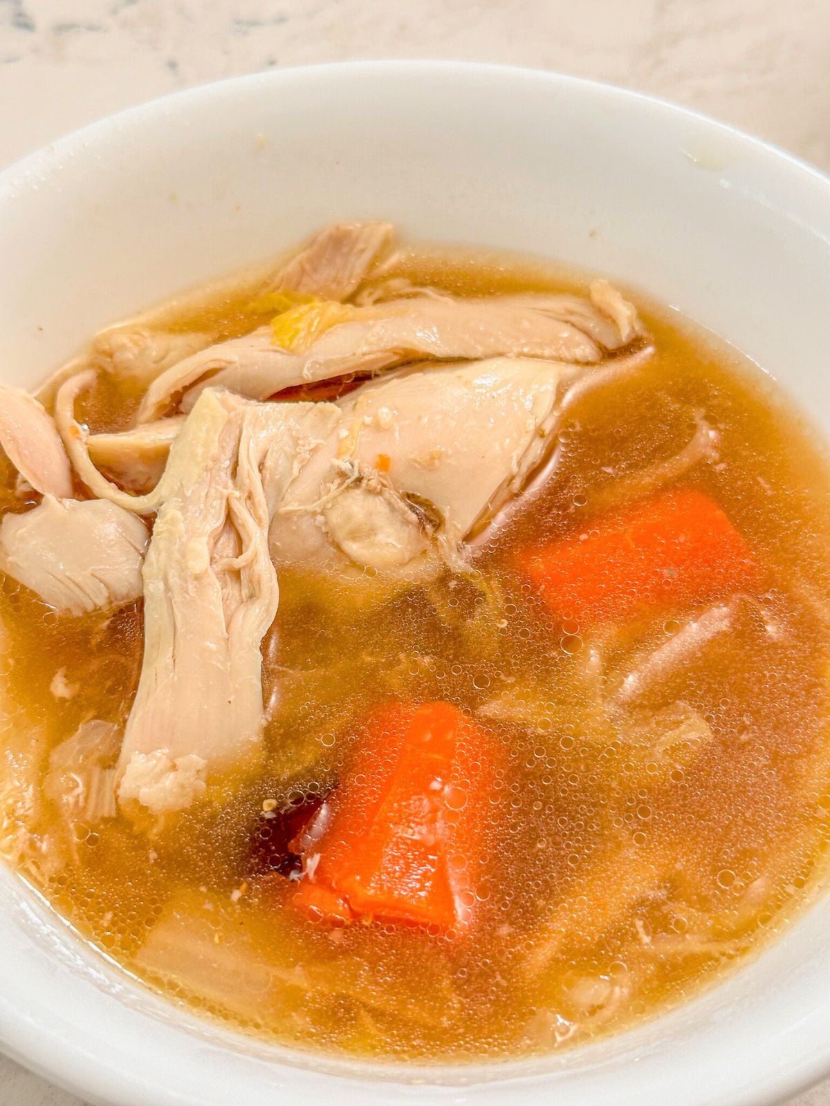 A bowl of soup filled with shredded chicken and chopped carrots.