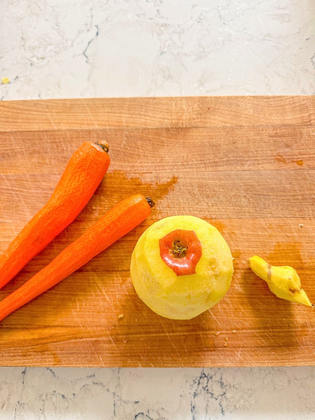 Peeled carrots, apple and ginger on a wooden chopping board.