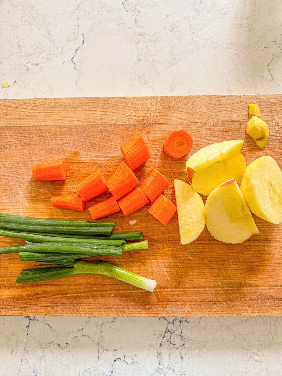 Sliced carrots, apple, ginger and green onions on a wooden chopping board.