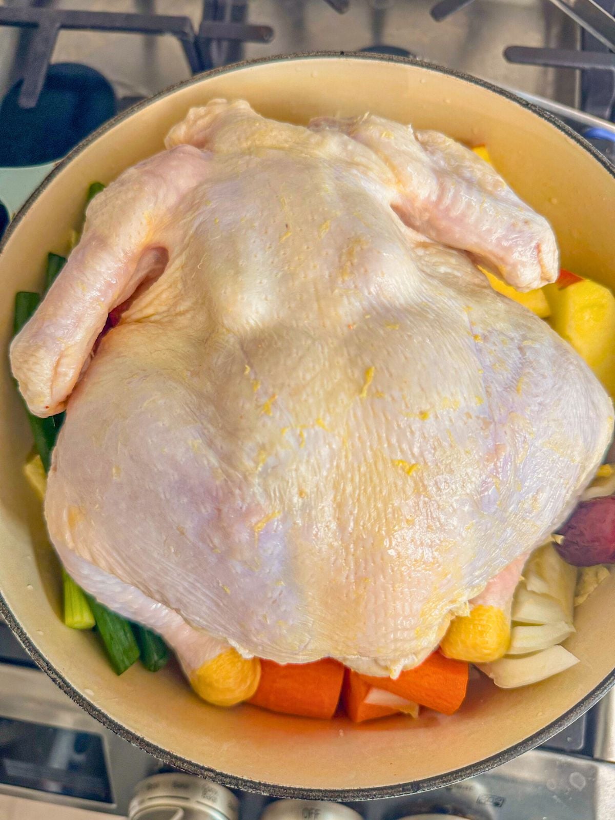 A whole raw chicken placed on top of a pot of mixed vegetables.