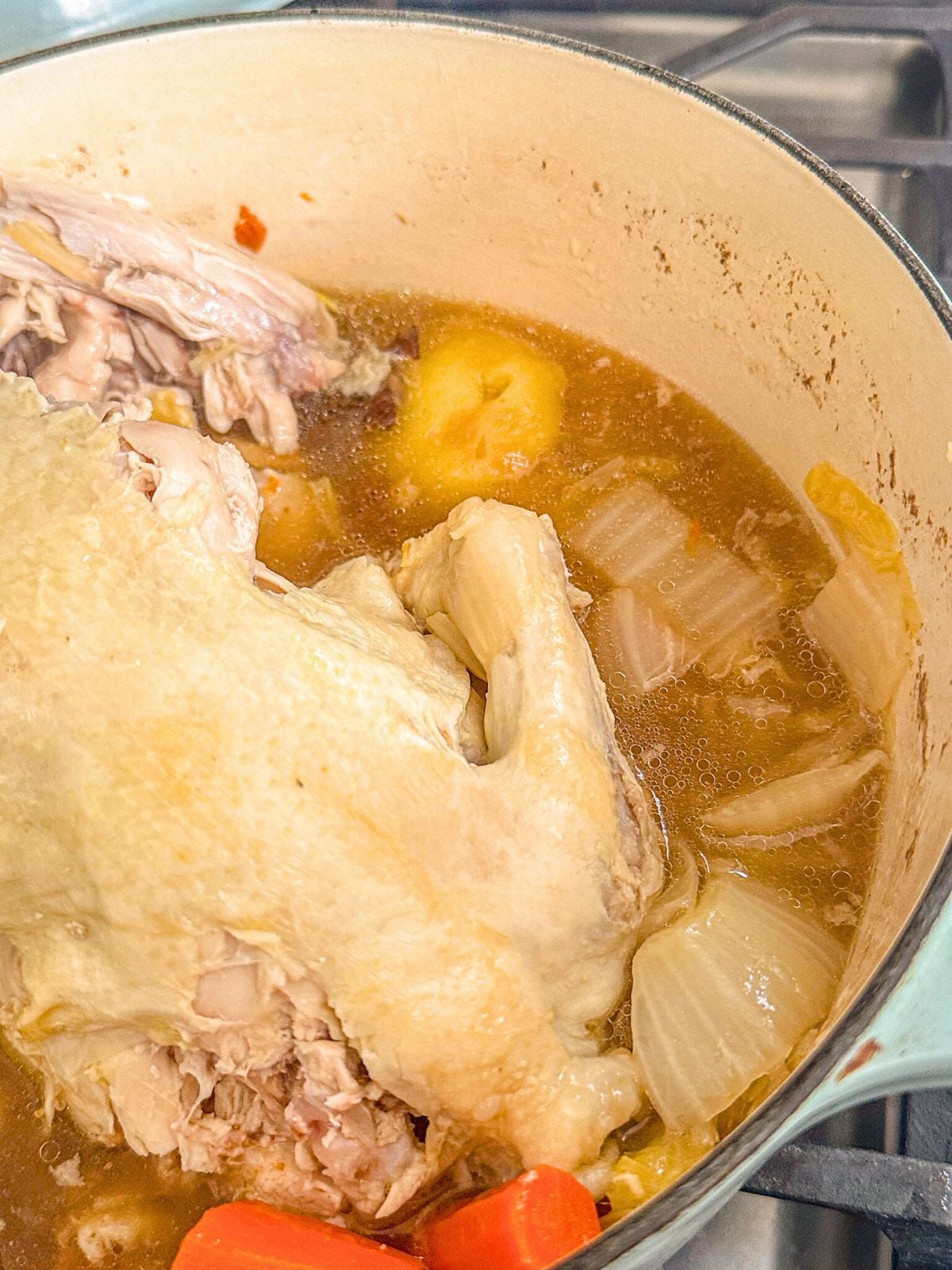 A whole cooked chicken with broth and mixed vegetables in a pot.