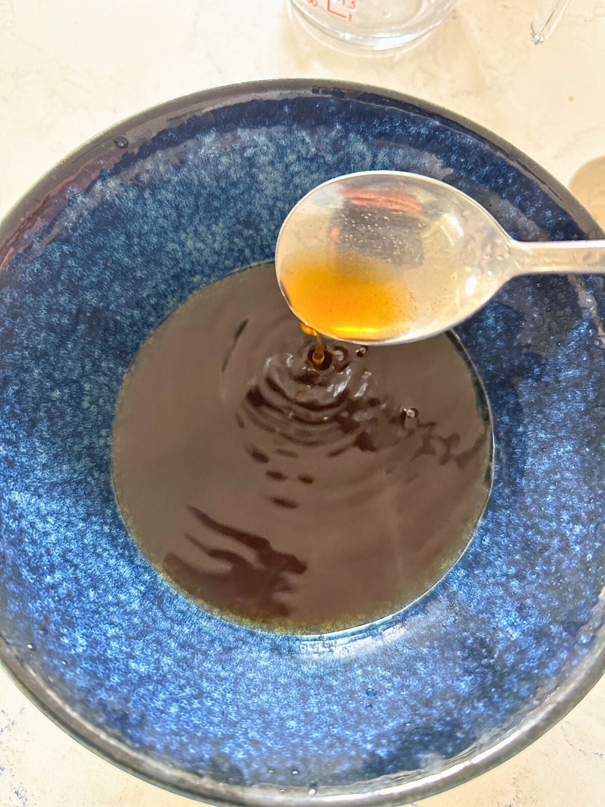 A bowl with soup base being mixed with hot water, dashi powder, soy sauce, and ponzu sauce using a spoon.