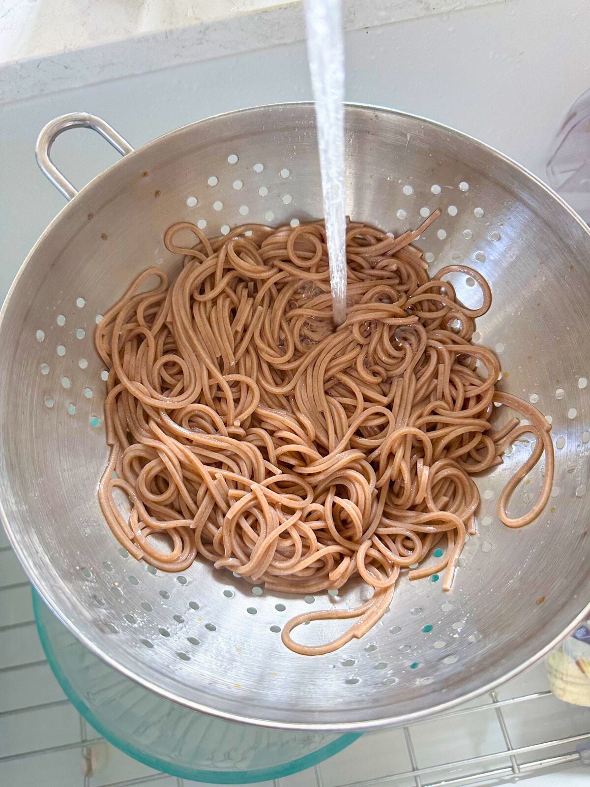 Coked soba noodles in a strainer with running water.