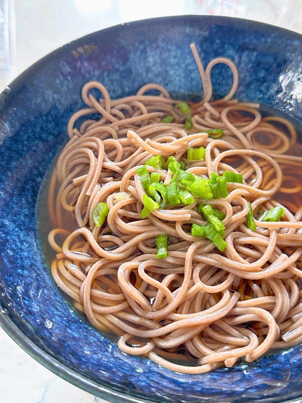 A bowl of cooked soba noodles topped with green onions.