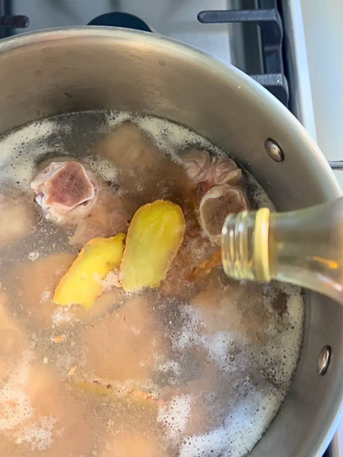 Pork knuckles in a pot of water with ginger slices and vinegar added.