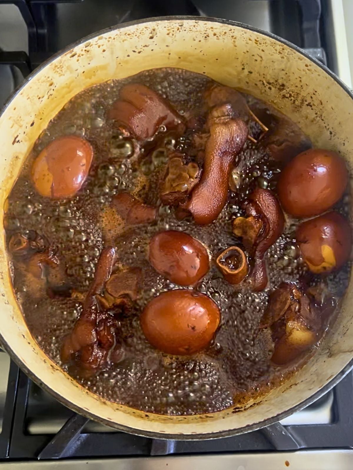 Pork knuckles and peeled eggs boiling in Chinese vinegar sauce in a large pot.