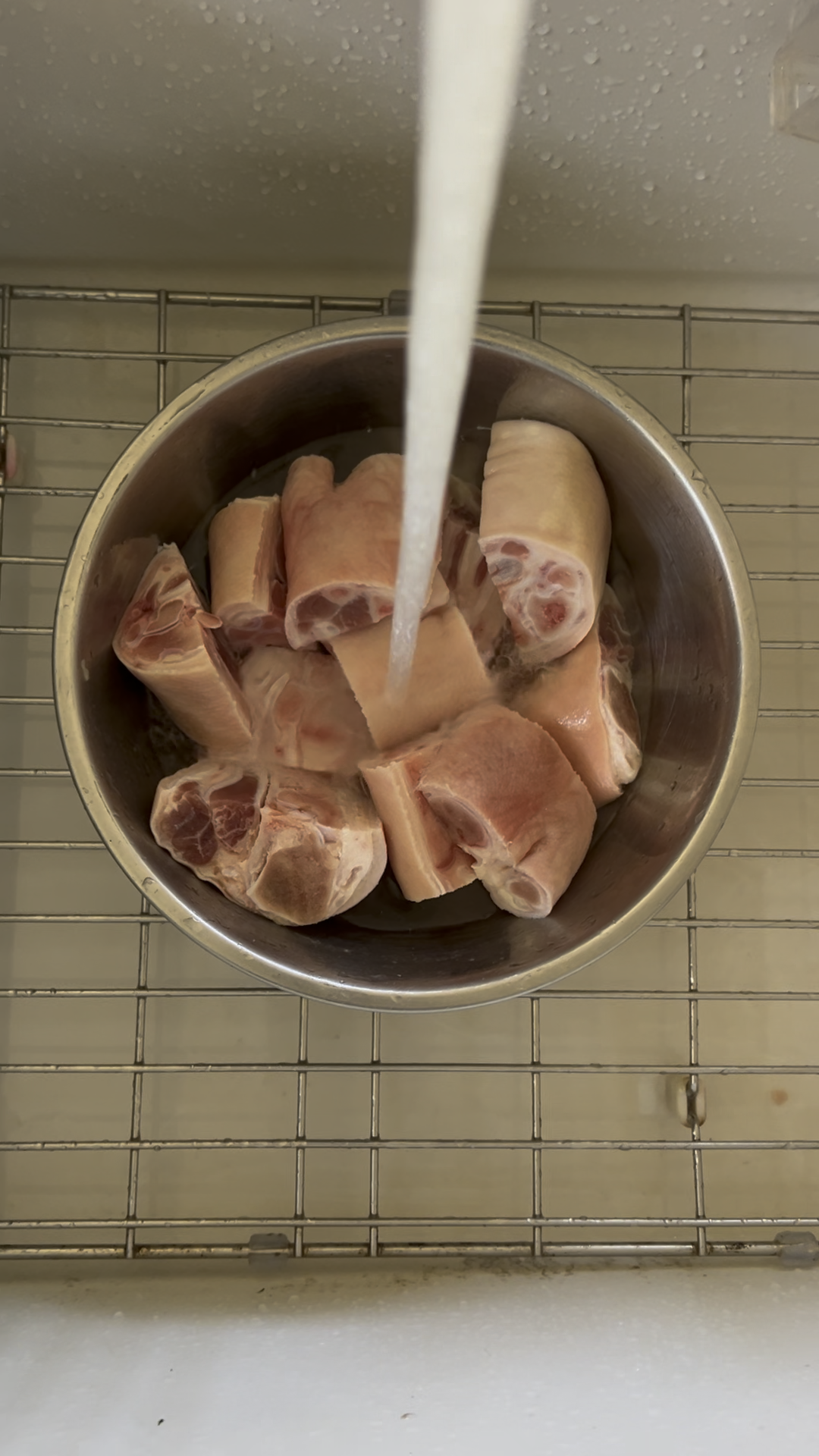 Pork knuckles in a metal bowl under running water.