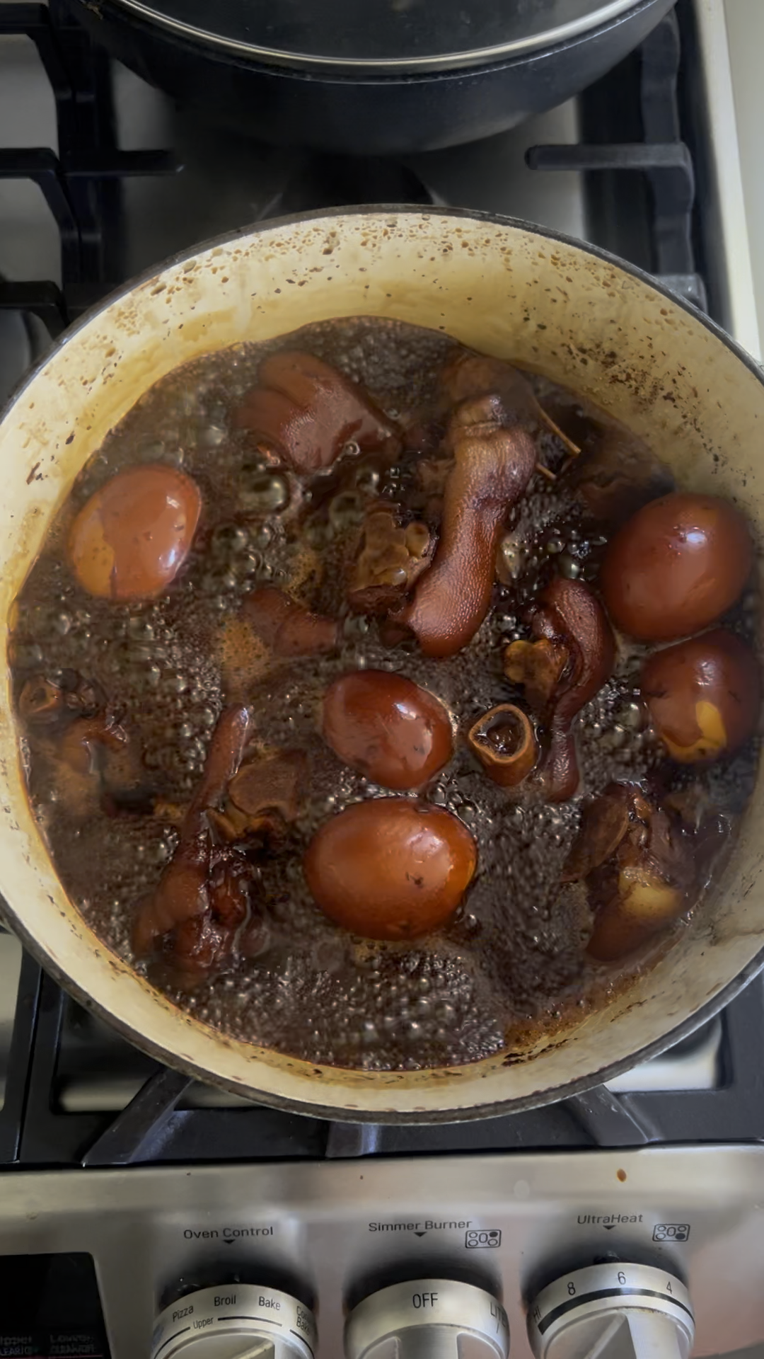 Pork knuckles and peeled eggs boiling in Chinese vinegar sauce in a large pot.