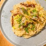 A plate of rice topped with cabbage, mushrooms, and sardines, garnished with sliced ginger and chopped green onions.