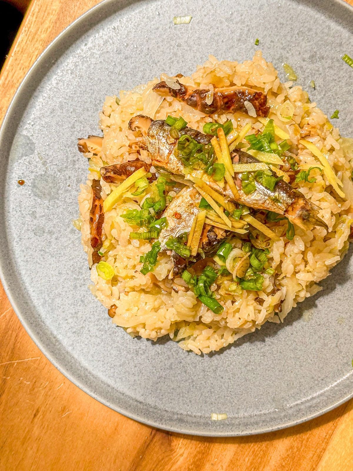 A plate of rice topped with cabbage, mushrooms, and sardines, garnished with sliced ginger and chopped green onions.