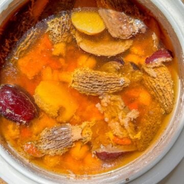 A pot of cooked Chinese postpartum soup with tender pork, mushrooms, jujube, ginger, and Chinese herbs.