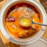 A pot of cooked postpartum soup with tender pork, mushrooms, jujube, ginger, and Chinese herbs being scooped with a spoon.