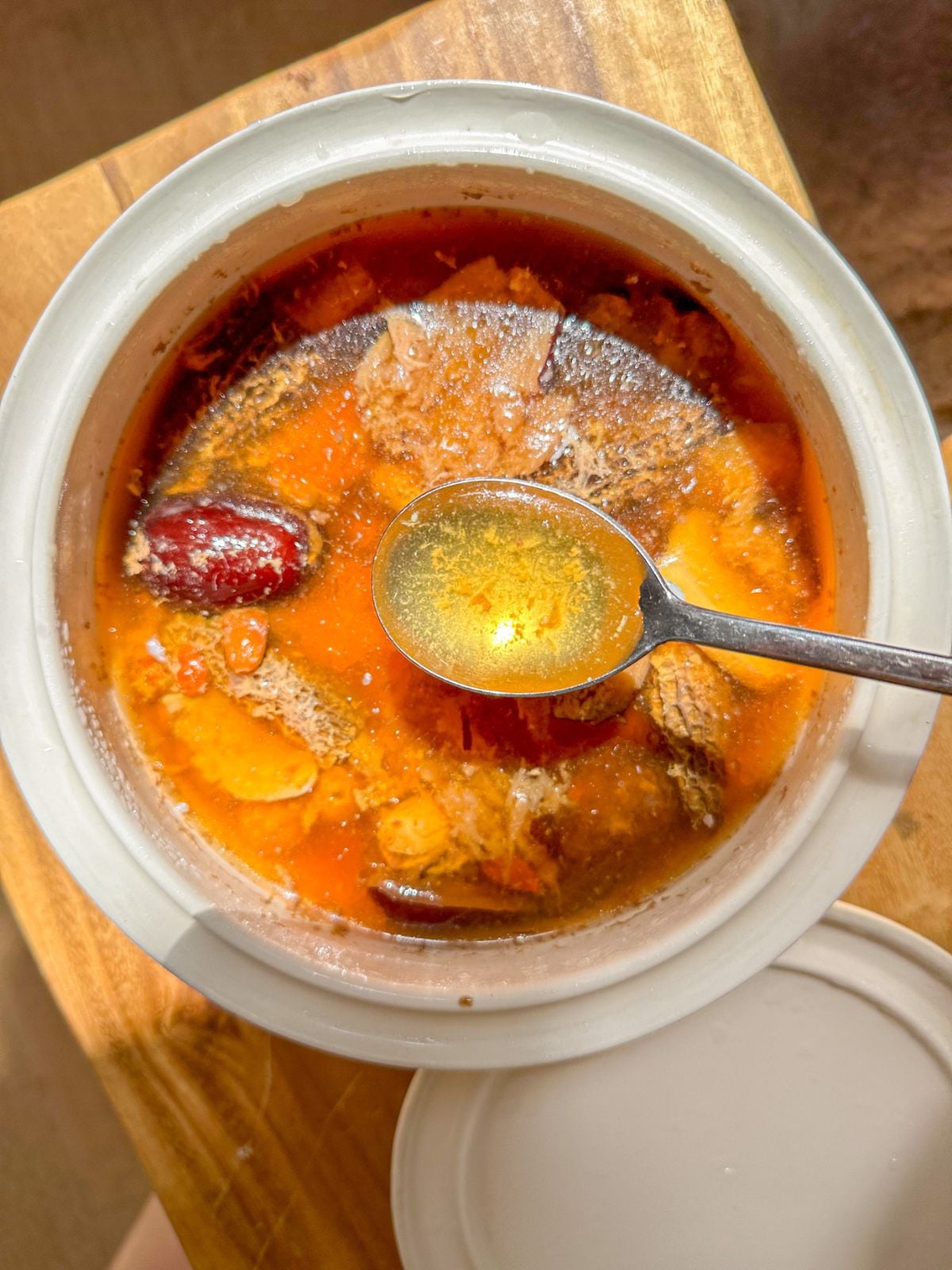 A pot of cooked postpartum soup with tender pork, mushrooms, jujube, ginger, and Chinese herbs being scooped with a spoon.