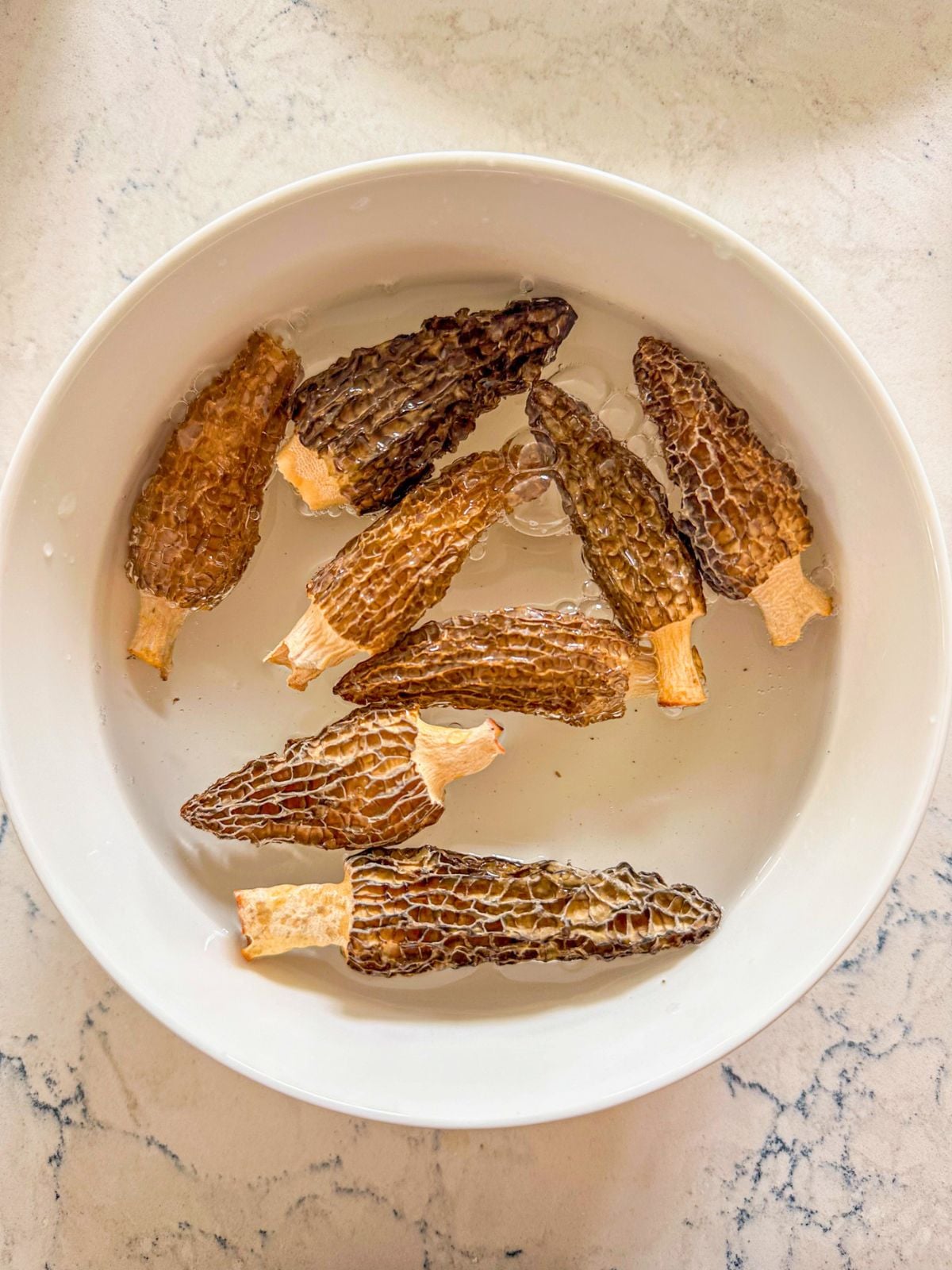 A bowl of morel mushrooms soaked in water.