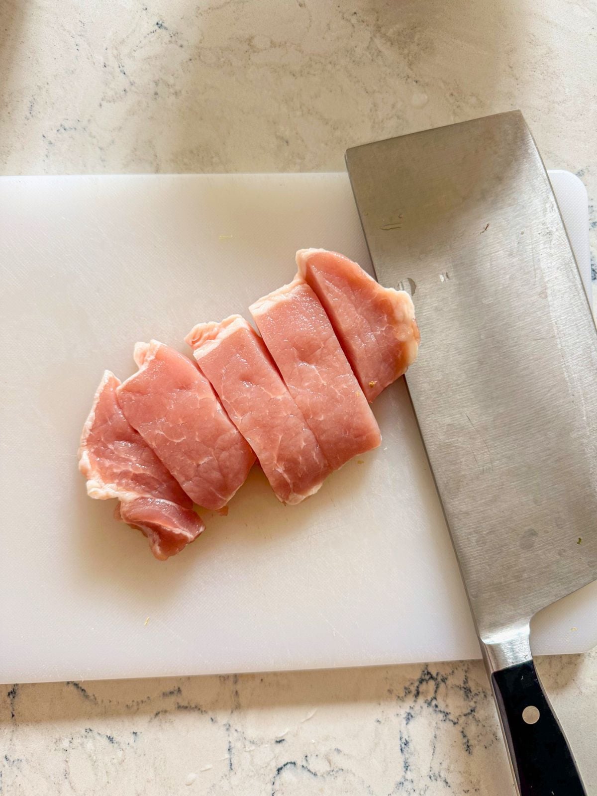 Sliced pork loin pieces on a cutting board beside a kitchen knife.