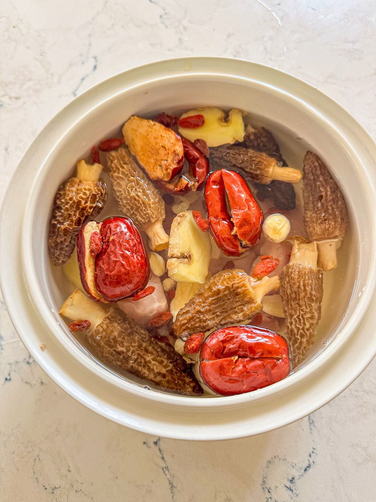 A pot with mushrooms, jujube, goji berries, ginger, and Chinese herbs soaked in water.