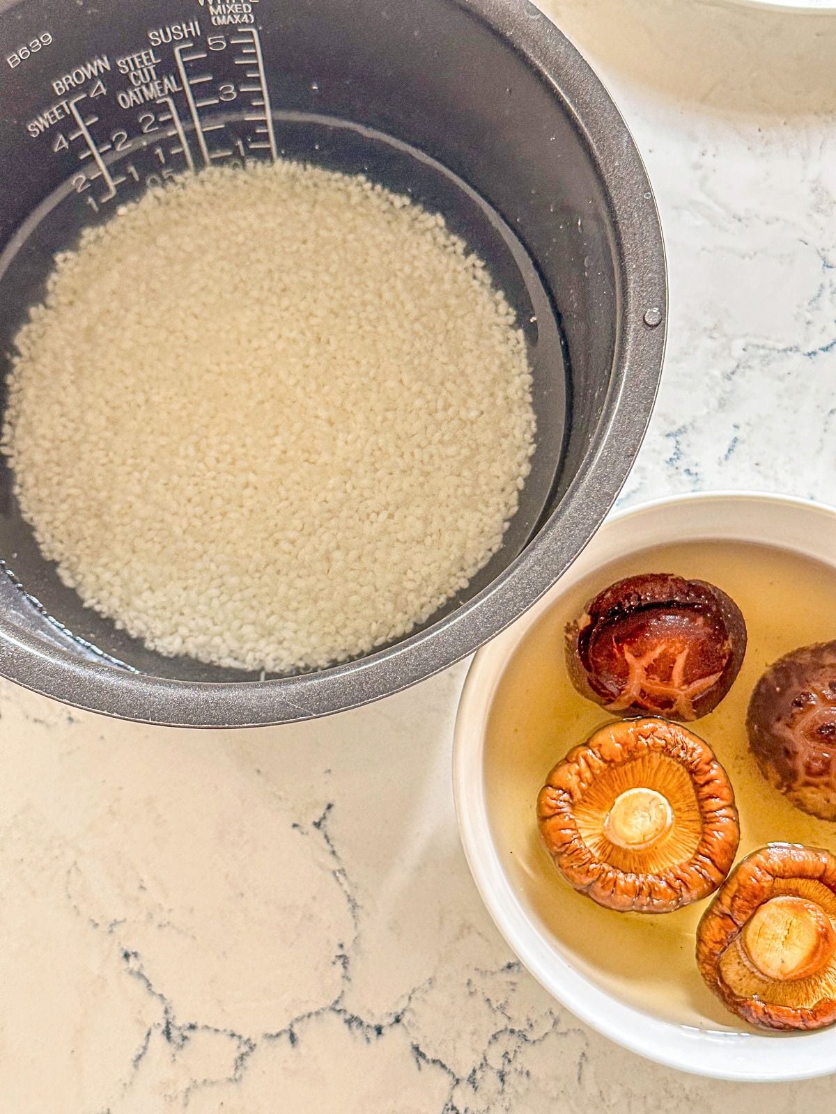 Soaked up rice in a pot next to a small white bowl with soaked mushrooms.