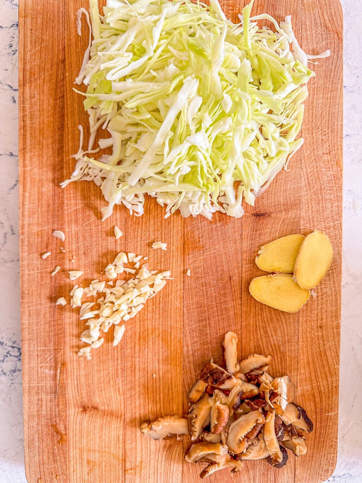 Sliced shiitake mushrooms, green cabbage, ginger and minced garlic on a chopping board.