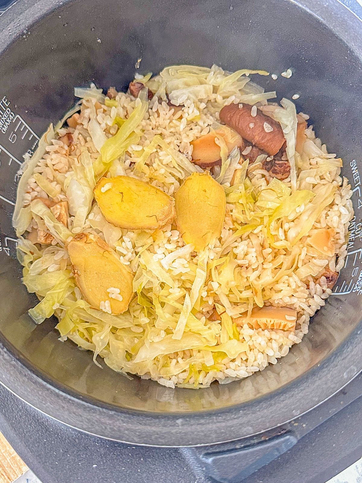 Cooked rice with sliced ginger, shiitake mushrooms and cabbage in a rice cooker.
