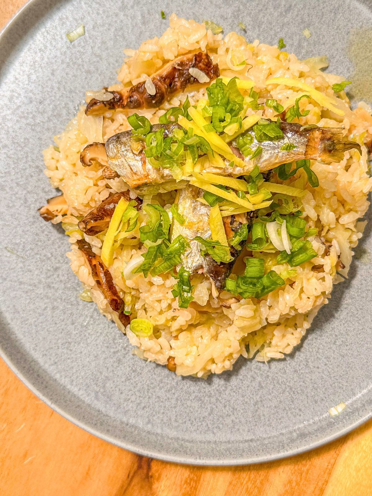 A plate of rice topped with cabbage, mushrooms, and sardines, garnished with sliced ginger and chopped green onions.