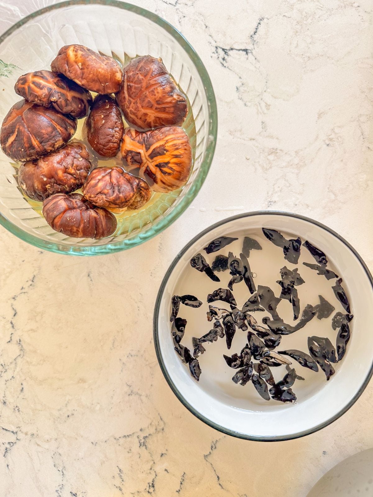 Wood ear mushrooms and shiitake mushrooms soaking separately in bowls of water.