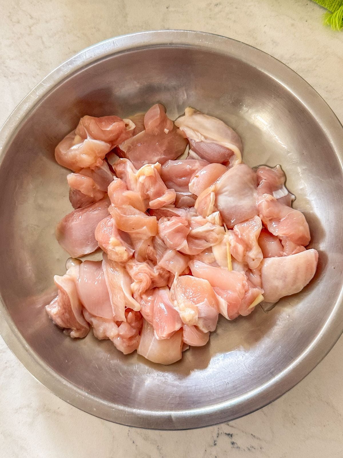 Raw chicken pieces in a metal mixing bowl.