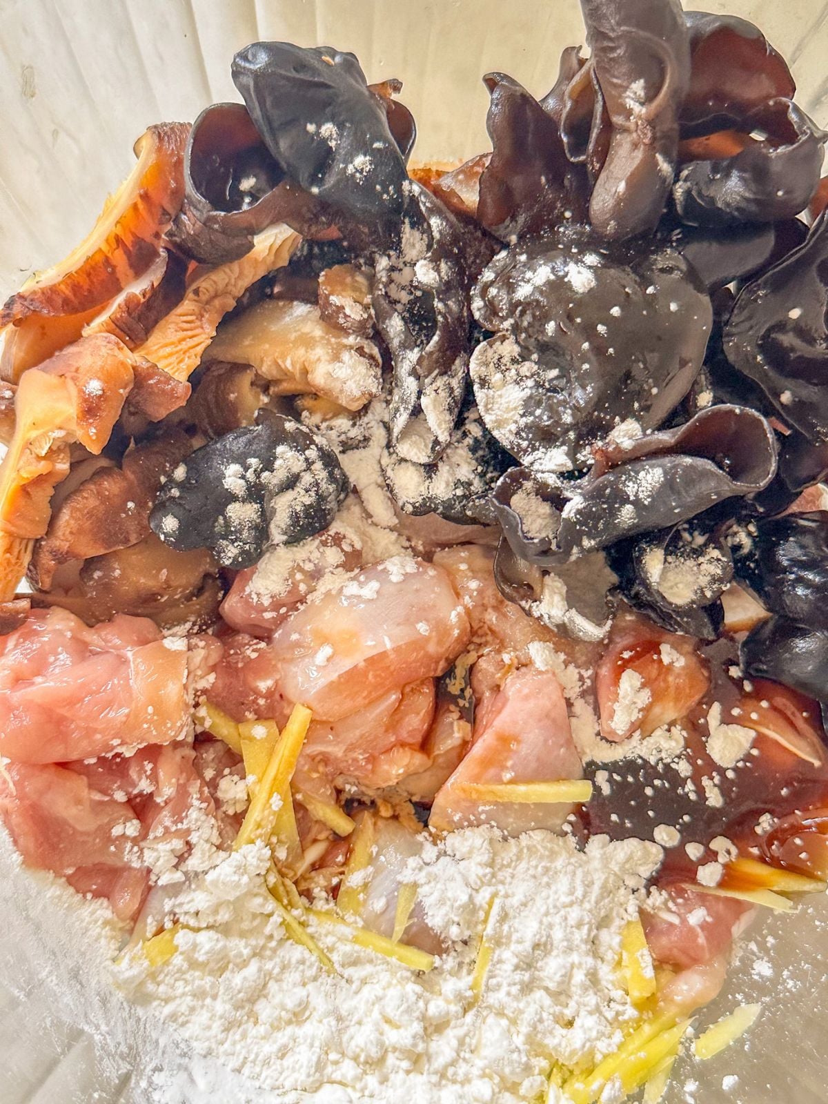 Chicken pieces in a bowl with shiitake mushrooms, wood ear mushrooms, ginger strips, chicken bouillon, chicken thigh, cornstarch, oyster sauce, soy sauce, salt and sugar.