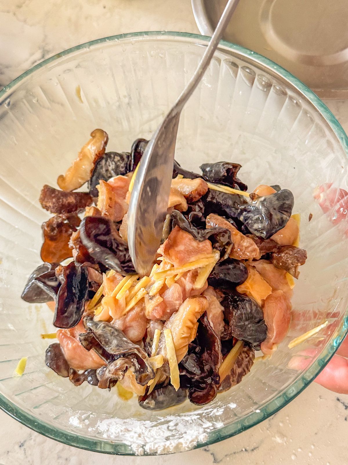 Mixing marinated chicken with a spoon until evenly coated.