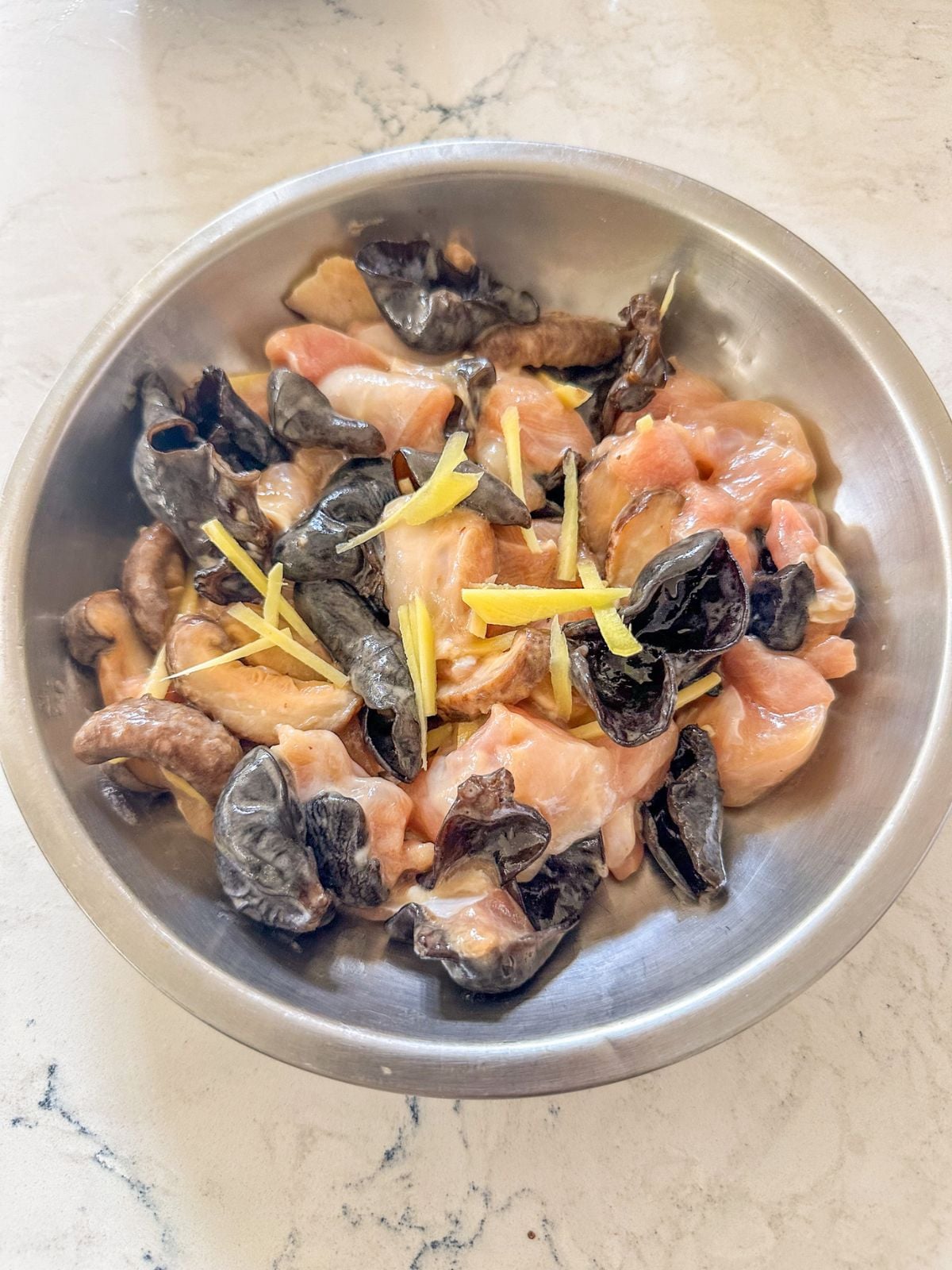 Prepared bowl of marinated chicken with sliced shiitake mushrooms, wood ear mushrooms, and ginger strips, ready to steam.