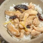 A bowl of white rice with steamed chicken, sliced shiitake mushrooms, wood ear mushrooms and ginger strips.