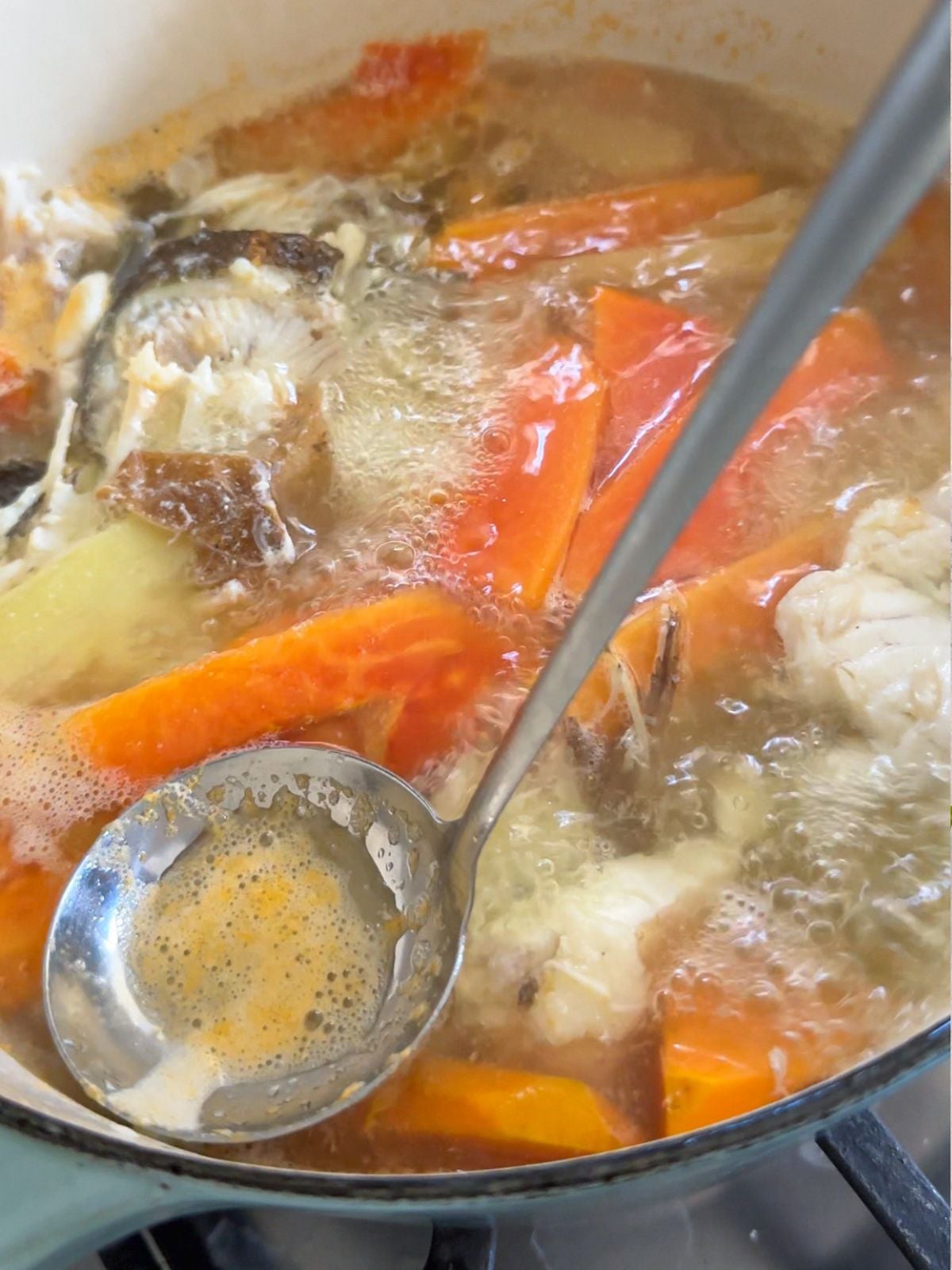 Fish bones boiling with water and papaya with a ladle skimming foam.