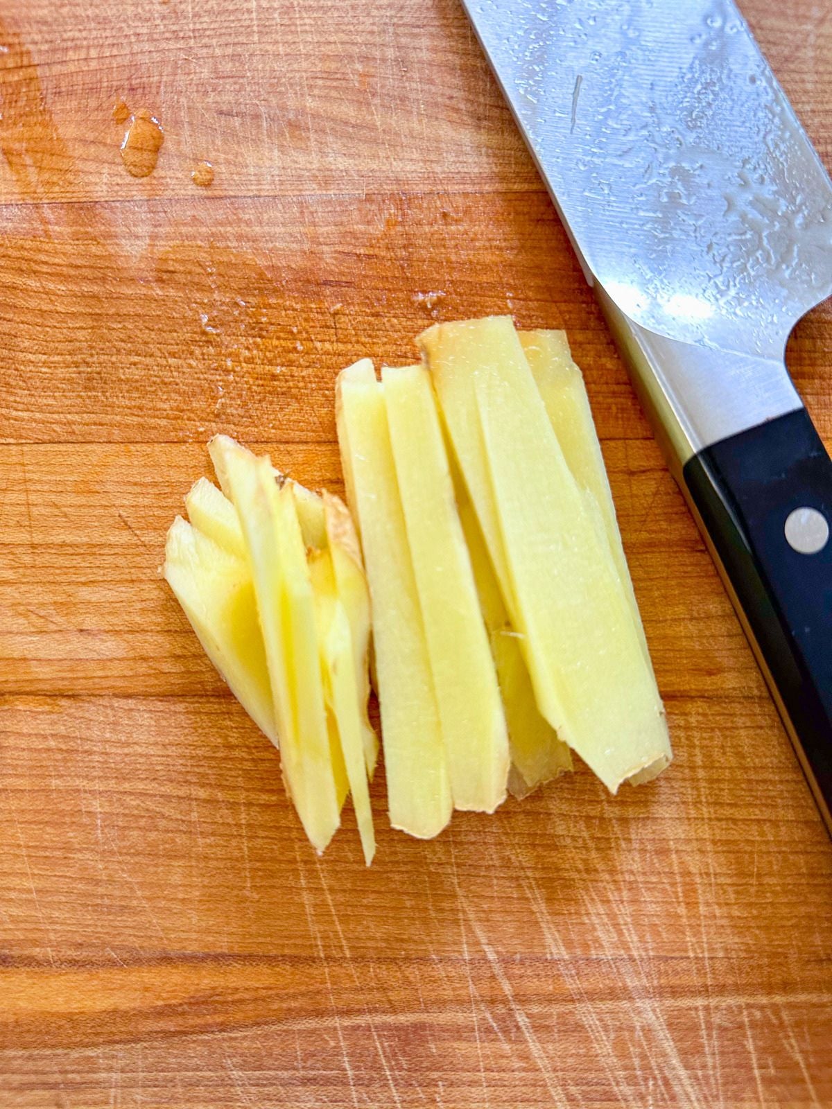 Sliced ginger on a cutting board beside a kitchen knife.