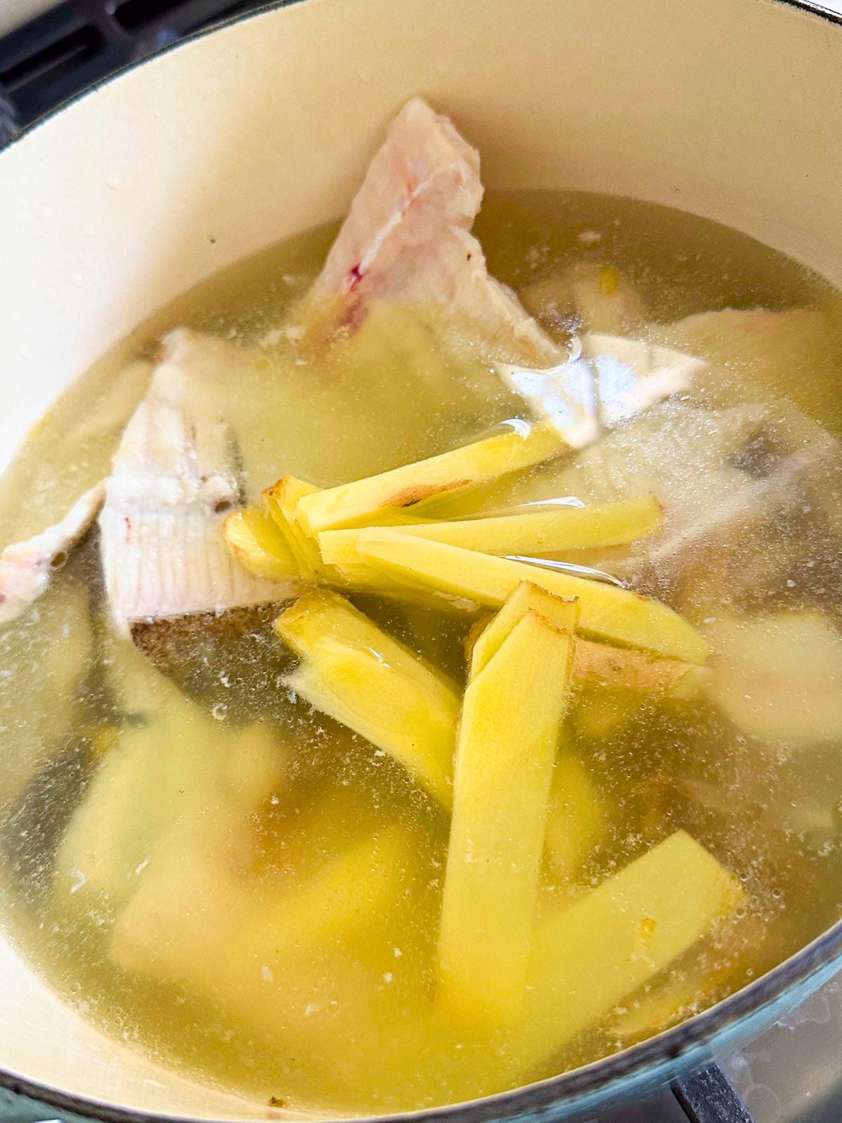 A pot filled with water, fish bones, and sliced ginger.