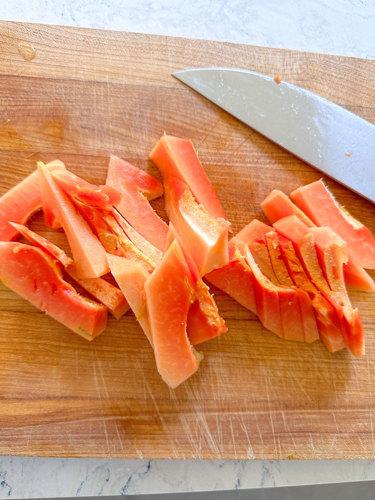 Papaya slices on a cutting board beside a kitchen knife.