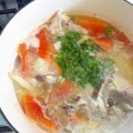 A pot with boiling water, fish bones, sliced ginger and papaya topped with cilantro.