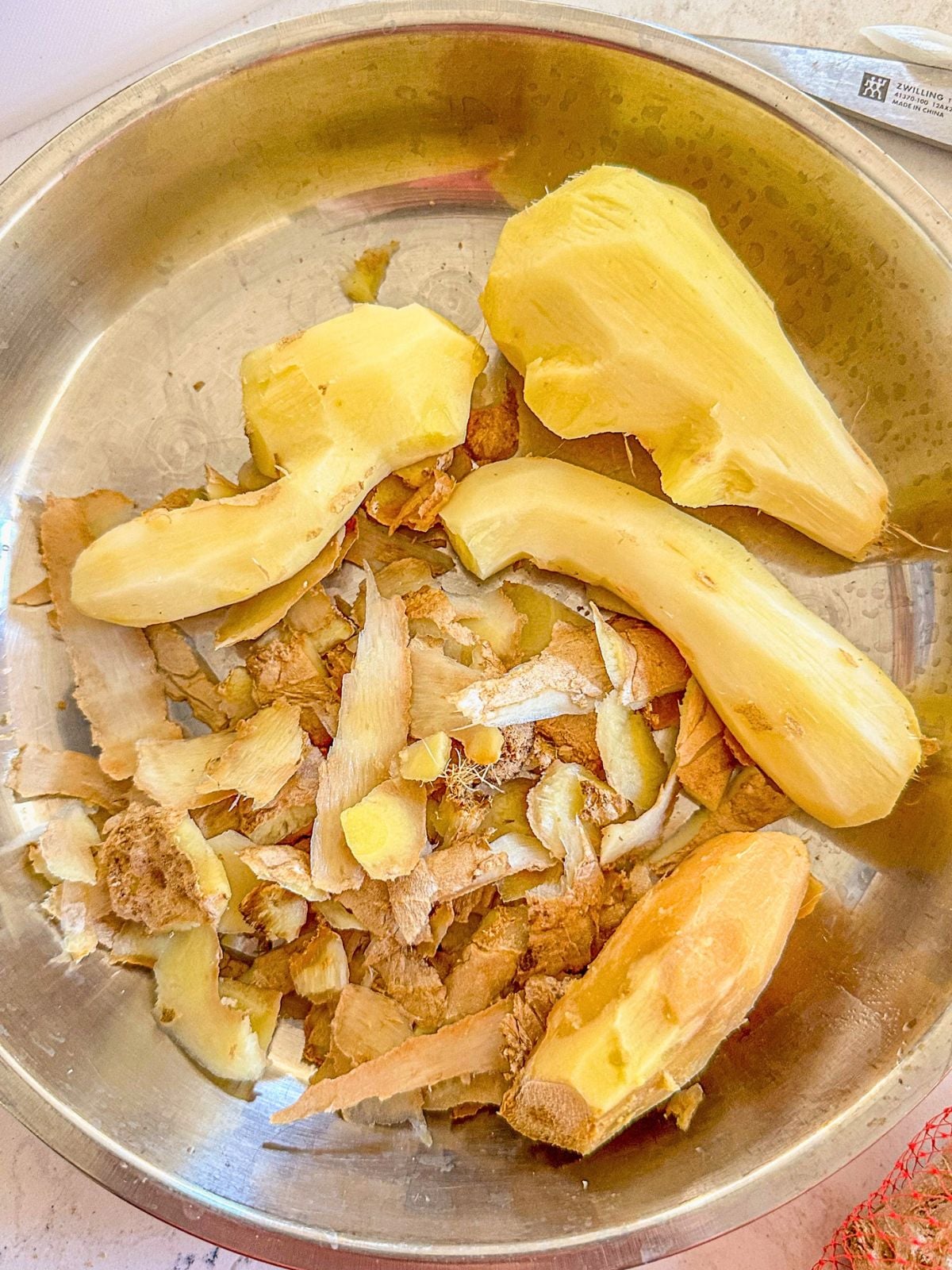 A bowl of peeled ginger chunks with ginger peelings beside it.
