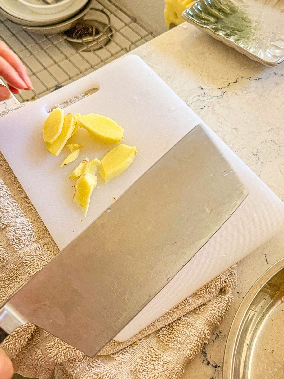 Sliced ginger pieces on a chopping board with a kitchen knife on the side.