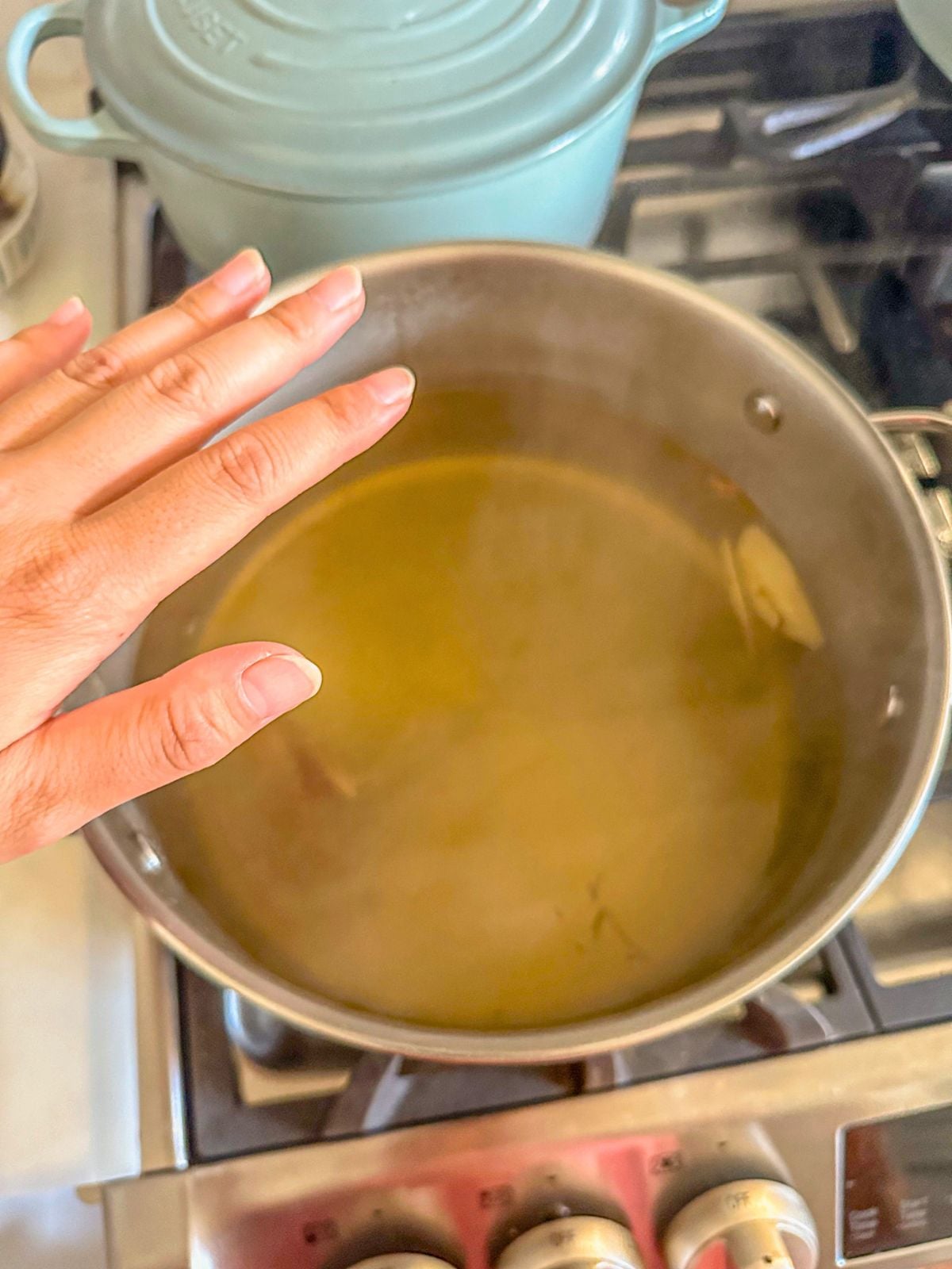 A hand checking the temperature of ginger water in a pot.
