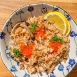 A plate of salmon and mushroom rice topped with green onions and fish roe, served with lemon slices on the side.