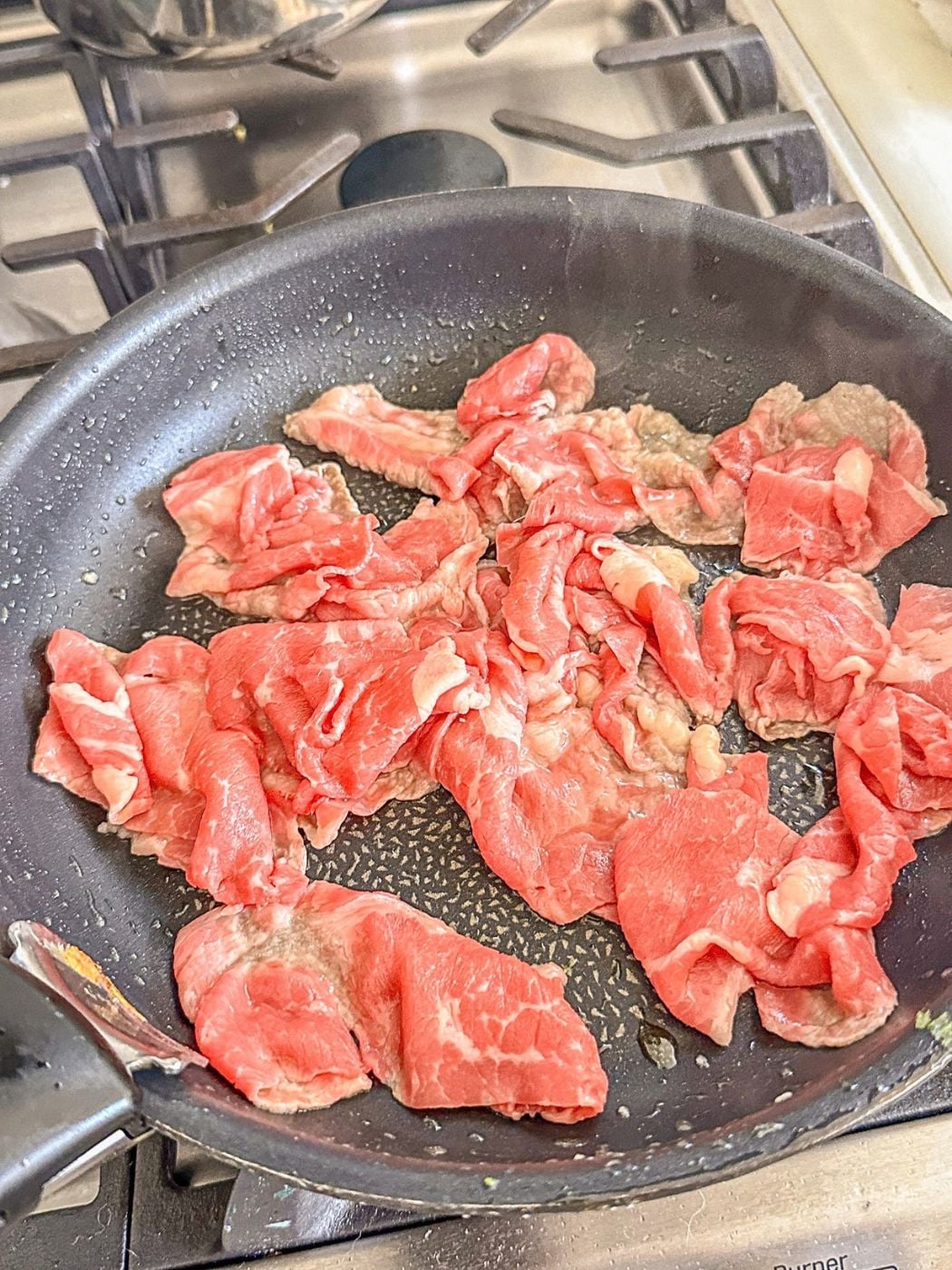 Thin slices of raw beef laid in a single layer in a skillet.