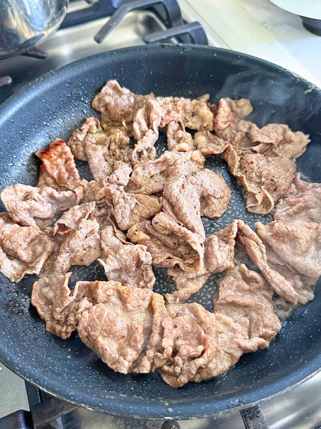 Browned slices of beef in a skillet after a few minutes of cooking.