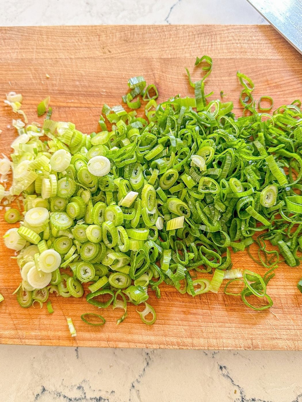 Thinly sliced green onions on a wooden cutting board.