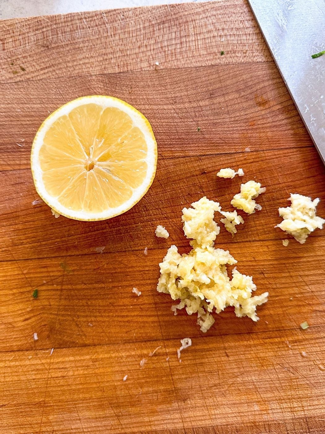 Grated garlic and a halved lemon on a wooden cutting board.