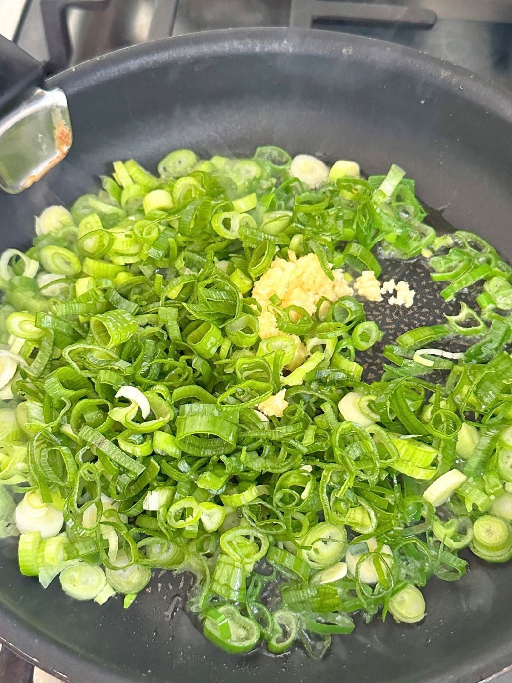 Sliced green onions and grated garlic cooking in oil in a skillet.