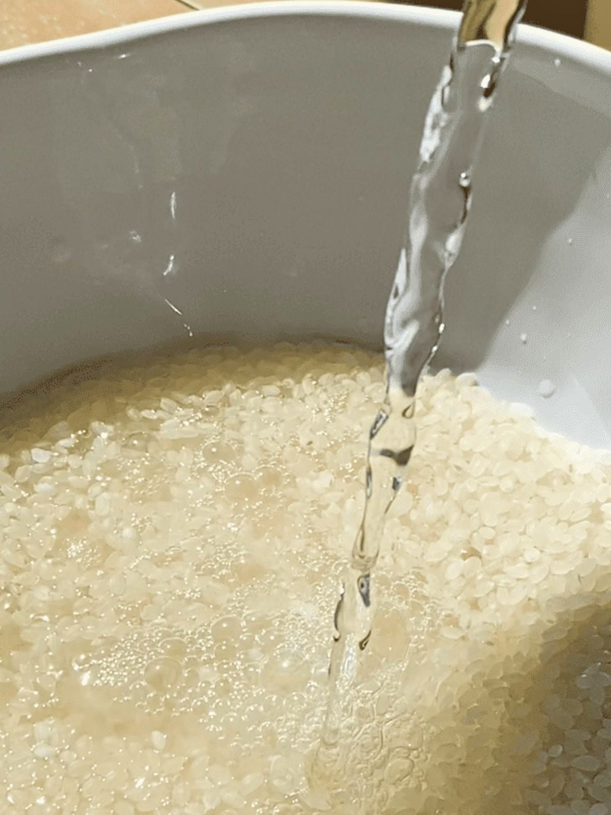 Short-grain rice rinsing under running water in a pot.