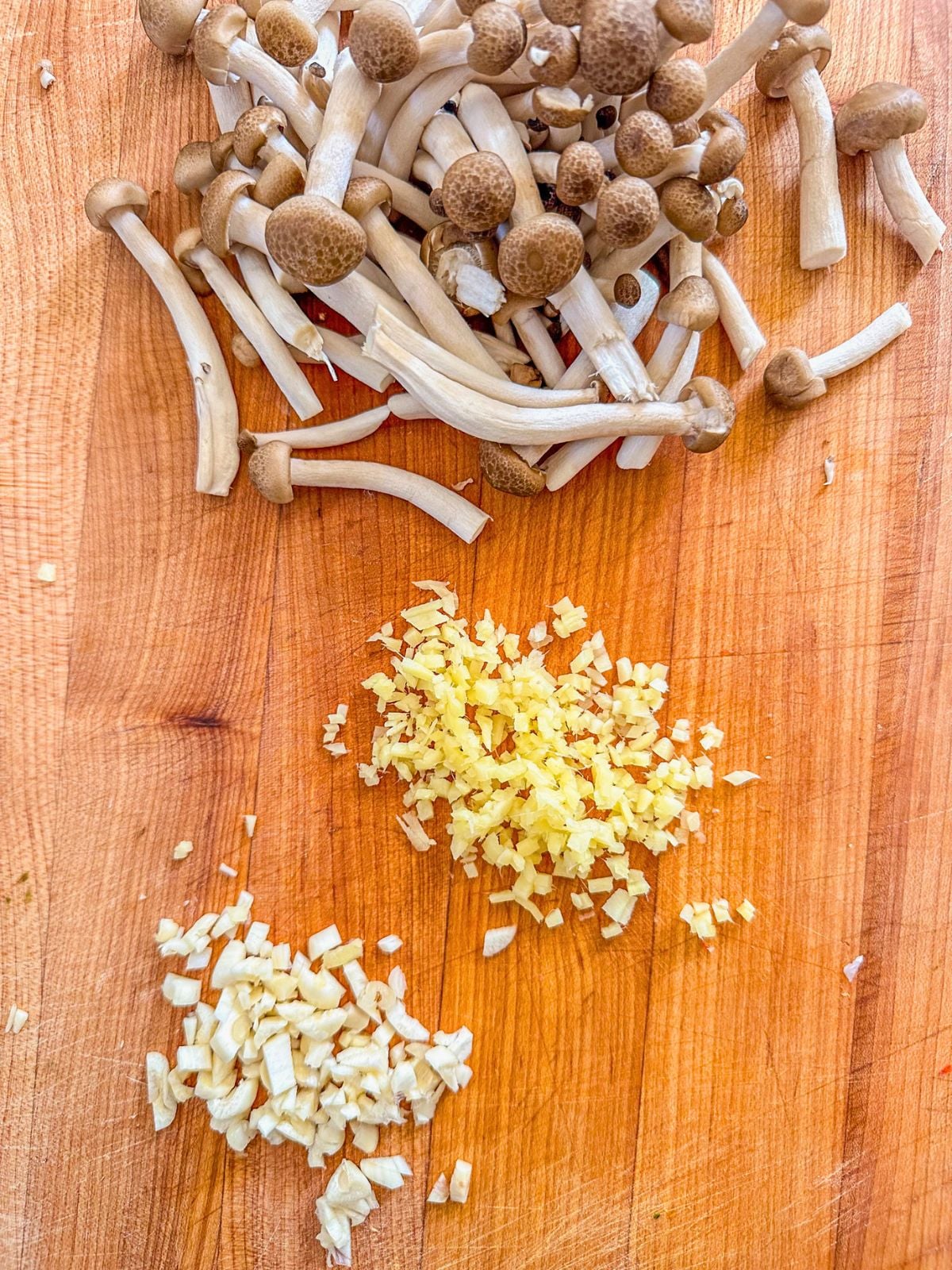 Chopped mushrooms, minced ginger, and garlic on a wooden cutting board.