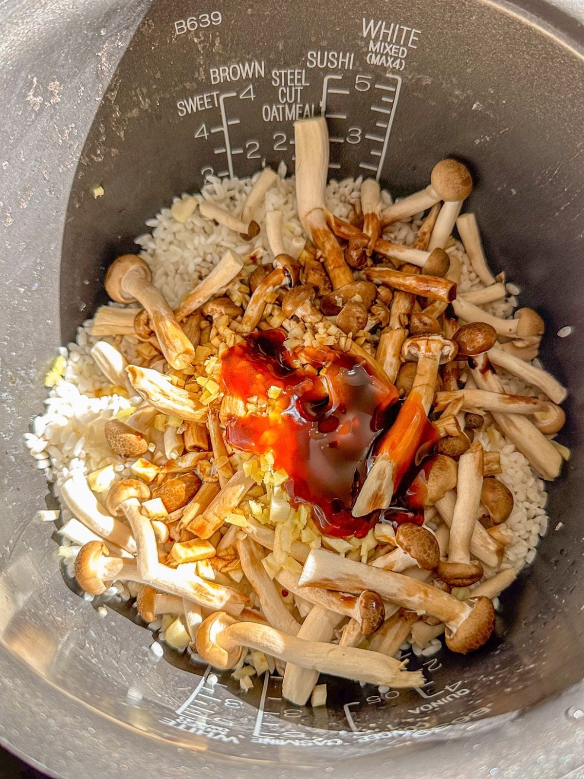 Washed rice in a pot with mushrooms, ginger, minced garlic, shallots, dark soy sauce, soy sauce, and oyster sauce.