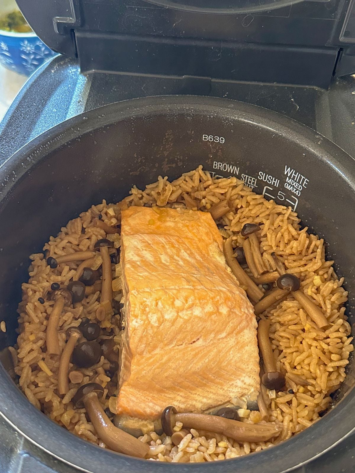 Cooked rice with mushrooms in a pot, topped with salmon in the center.